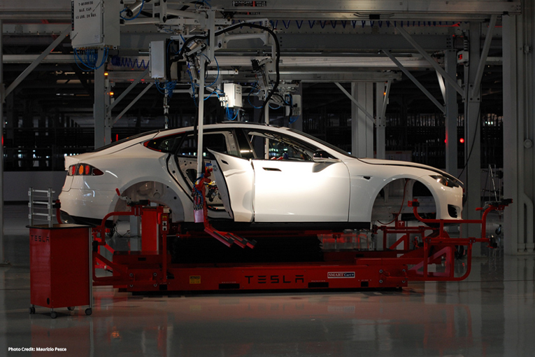 Una Tesla model S bianca in linea di montaggio. Si vedono solo la carrozzeria ed il telaio.
